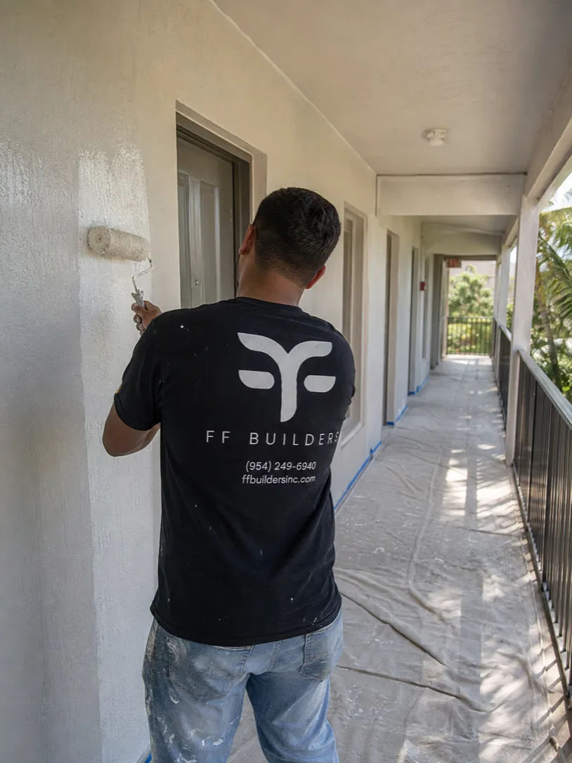 Painter repainting a condominium corridor with floors covered and door frames masked