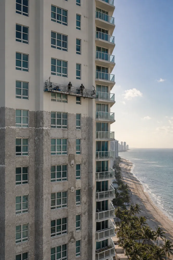 Oceanfront condominium tower mid-repaint, fresh paint above weathered concrete below